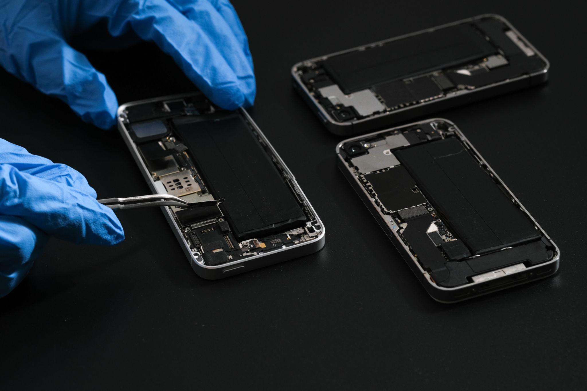 Person wearing blue gloves repairing a smartphone on a black background